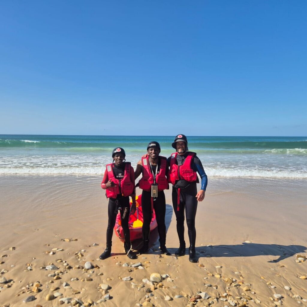 Image of people in wetsuits on the beach with a kayak